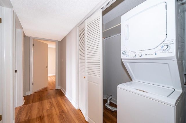 laundry area featuring light hardwood / wood-style floors, stacked washer / drying machine, and a textured ceiling