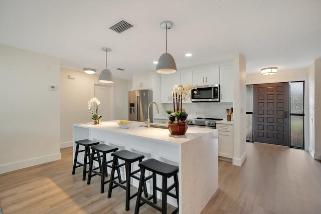 kitchen featuring pendant lighting, stainless steel appliances, an island with sink, white cabinetry, and sink