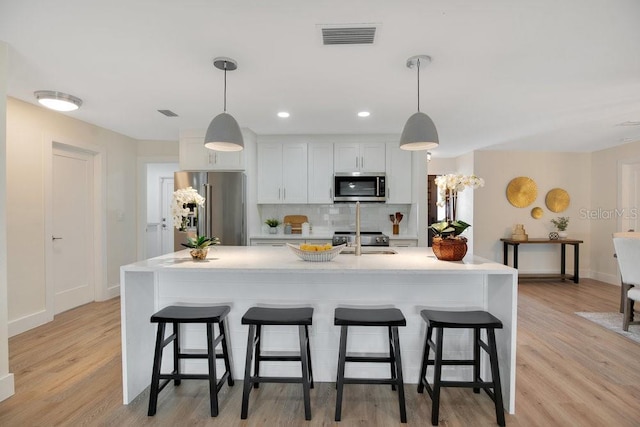 kitchen with stainless steel appliances, white cabinetry, decorative light fixtures, and an island with sink