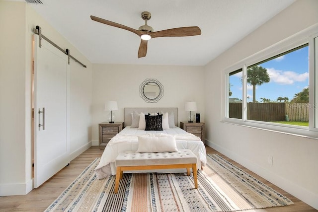 bedroom featuring ceiling fan, a barn door, and light hardwood / wood-style flooring