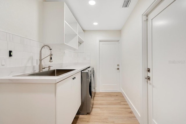 laundry room featuring washing machine and dryer, cabinets, light hardwood / wood-style flooring, and sink