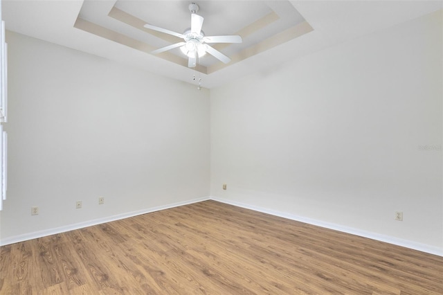 empty room featuring ceiling fan, light hardwood / wood-style flooring, and a raised ceiling