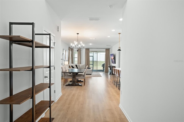 corridor with light hardwood / wood-style flooring and an inviting chandelier