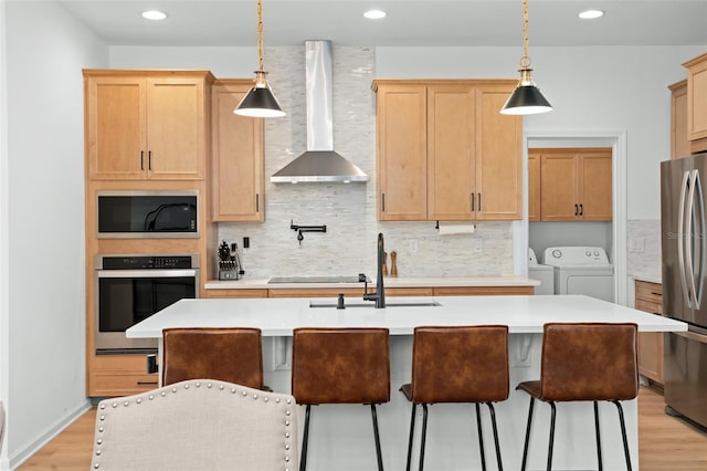 kitchen featuring stainless steel appliances, a kitchen island with sink, decorative light fixtures, and wall chimney range hood