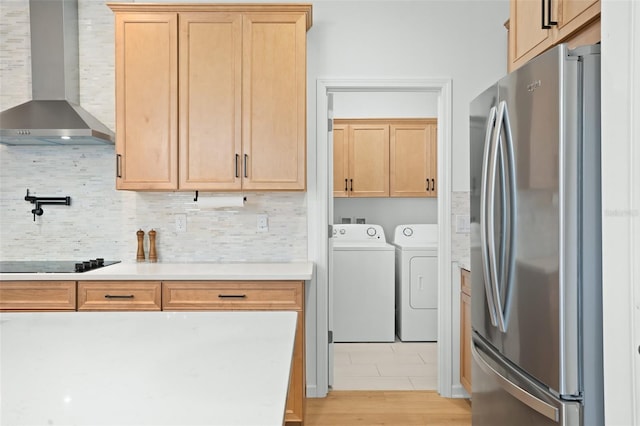 interior space featuring stainless steel fridge, washer and dryer, black electric cooktop, tasteful backsplash, and wall chimney exhaust hood