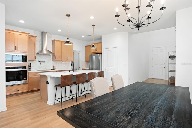 kitchen featuring light hardwood / wood-style flooring, wall chimney range hood, stainless steel appliances, a breakfast bar, and a center island with sink