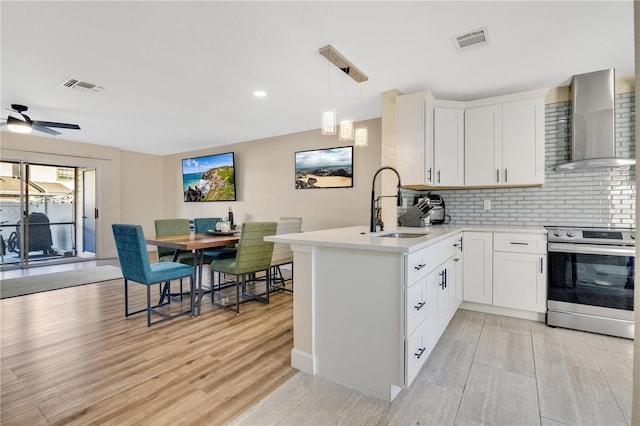 kitchen featuring stainless steel electric stove, white cabinetry, kitchen peninsula, hanging light fixtures, and wall chimney range hood