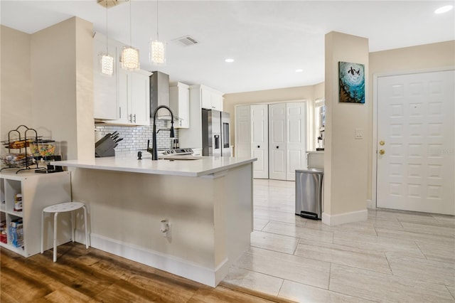 kitchen featuring kitchen peninsula, pendant lighting, a kitchen bar, stainless steel refrigerator with ice dispenser, and white cabinetry