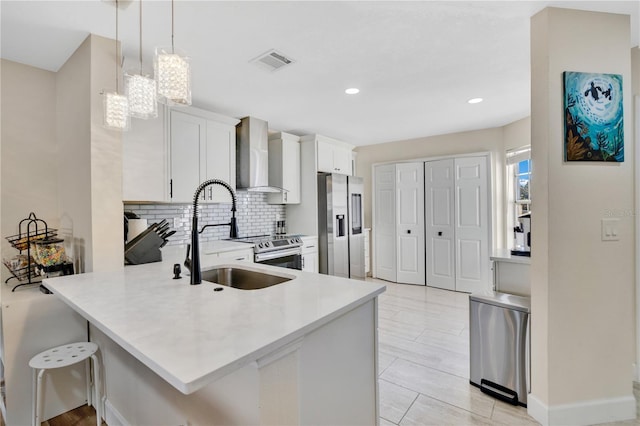 kitchen with decorative light fixtures, stainless steel appliances, wall chimney range hood, decorative backsplash, and white cabinets