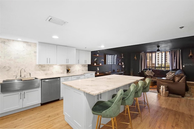 kitchen featuring white cabinets, a center island, light hardwood / wood-style floors, backsplash, and stainless steel dishwasher