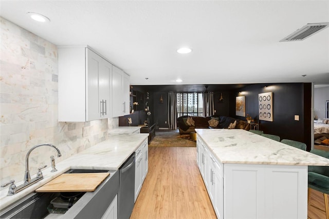 kitchen with dishwasher, a kitchen island, white cabinetry, tasteful backsplash, and light stone counters