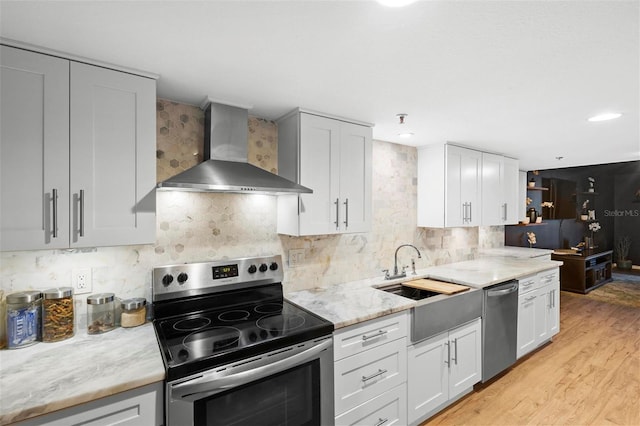 kitchen featuring white cabinets, wall chimney exhaust hood, appliances with stainless steel finishes, a sink, and backsplash