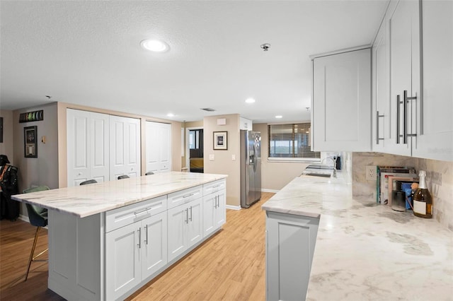 kitchen with light stone counters, a breakfast bar area, white cabinetry, light wood-type flooring, and stainless steel fridge