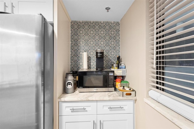 kitchen featuring light countertops, backsplash, freestanding refrigerator, and white cabinetry