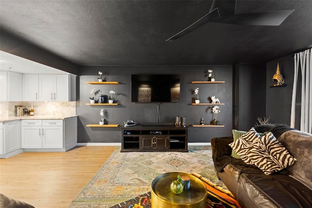 living area featuring light wood-type flooring, a textured ceiling, and baseboards