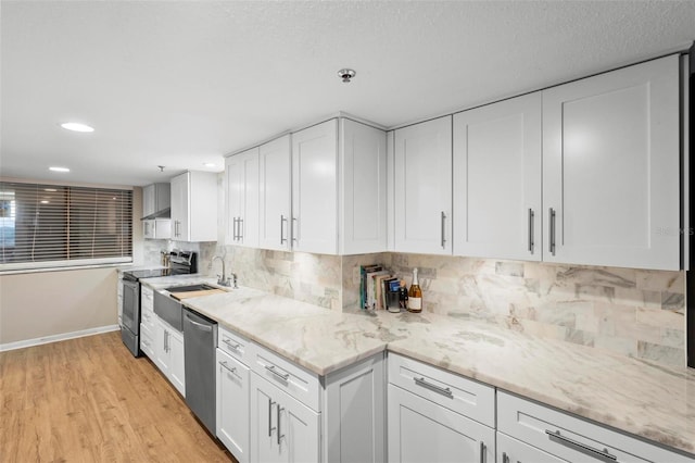 kitchen with a sink, white cabinets, appliances with stainless steel finishes, decorative backsplash, and light wood finished floors