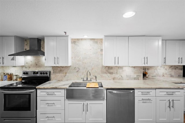 kitchen featuring appliances with stainless steel finishes, white cabinetry, a sink, and wall chimney range hood