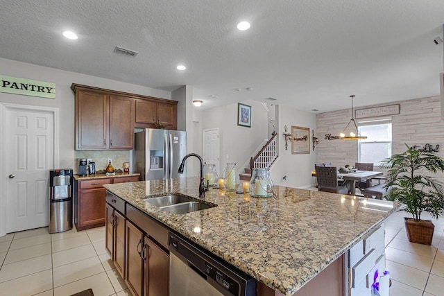 kitchen with sink, light tile patterned floors, stainless steel appliances, light stone counters, and an island with sink