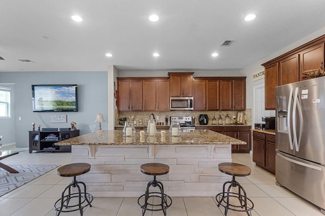 kitchen featuring stainless steel appliances, a kitchen island with sink, a breakfast bar area, and light tile patterned floors