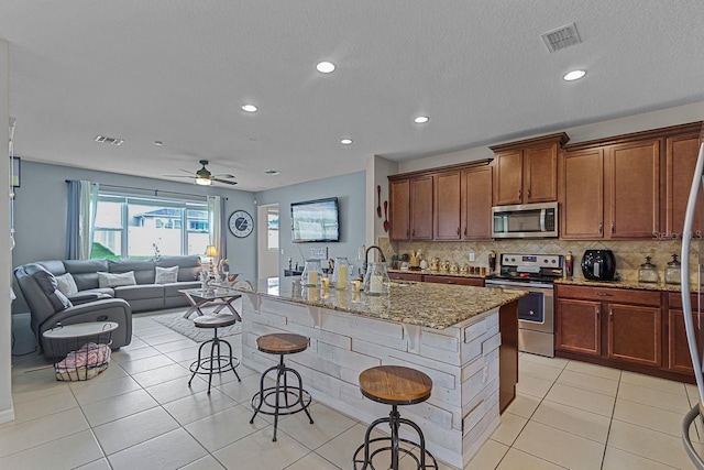 kitchen with stainless steel appliances, a kitchen breakfast bar, light stone countertops, and a center island with sink