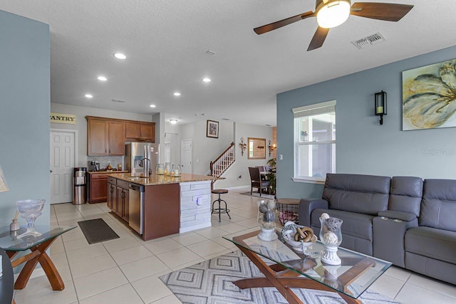 kitchen with a breakfast bar area, stainless steel appliances, light stone countertops, an island with sink, and light tile patterned flooring