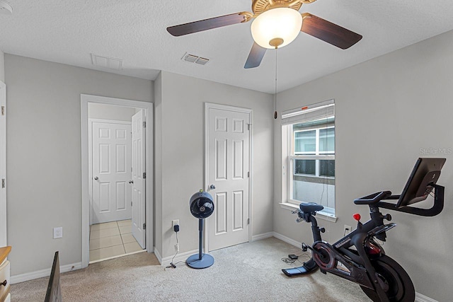 workout area featuring ceiling fan, light colored carpet, and a textured ceiling