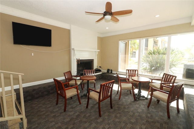 dining area with ceiling fan, dark colored carpet, a brick fireplace, and ornamental molding