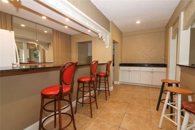 bar featuring white cabinets, light tile patterned floors, and a textured ceiling