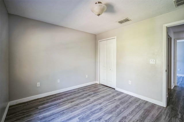 unfurnished bedroom with a textured ceiling, dark wood-type flooring, and a closet