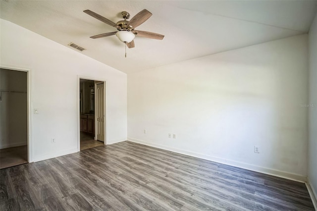 unfurnished bedroom featuring a closet, ceiling fan, dark wood-type flooring, a walk in closet, and lofted ceiling