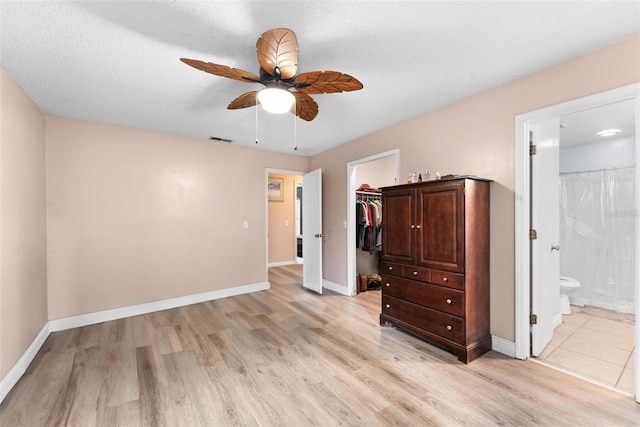 unfurnished bedroom with ceiling fan, connected bathroom, light wood-type flooring, a closet, and a walk in closet