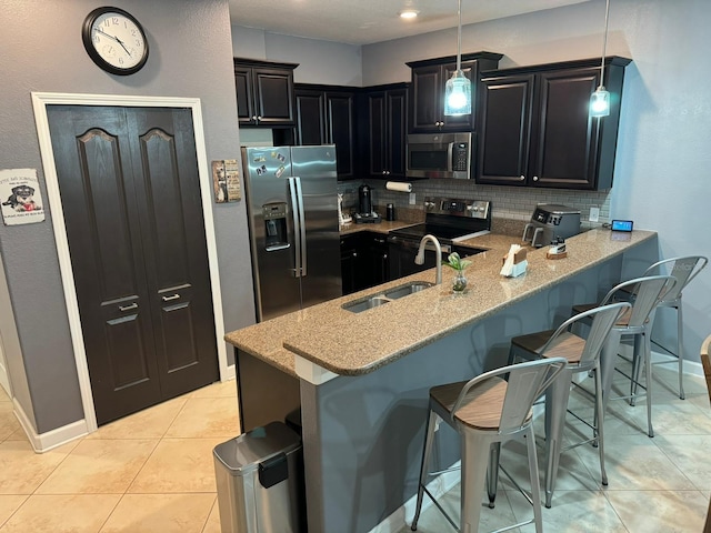 kitchen featuring kitchen peninsula, appliances with stainless steel finishes, a kitchen breakfast bar, hanging light fixtures, and sink