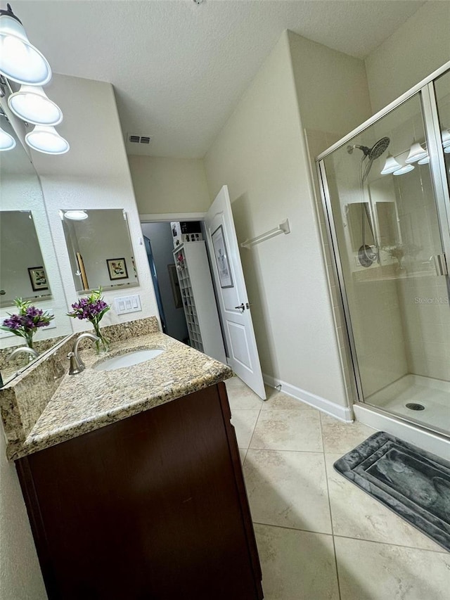 bathroom with a textured ceiling, a shower with door, tile patterned floors, and vanity