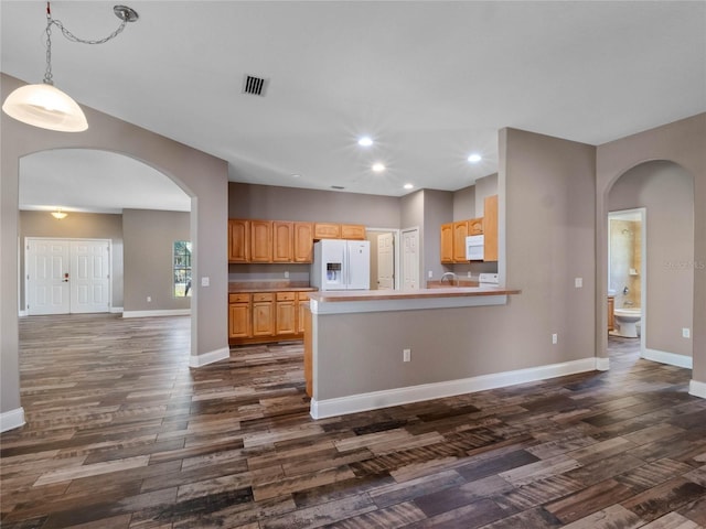 kitchen with decorative light fixtures, white appliances, kitchen peninsula, light brown cabinetry, and dark wood-type flooring