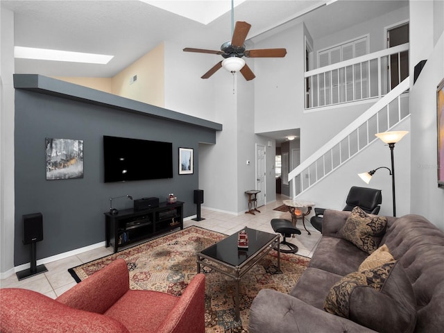 living area with light tile patterned floors, ceiling fan, a skylight, baseboards, and stairs