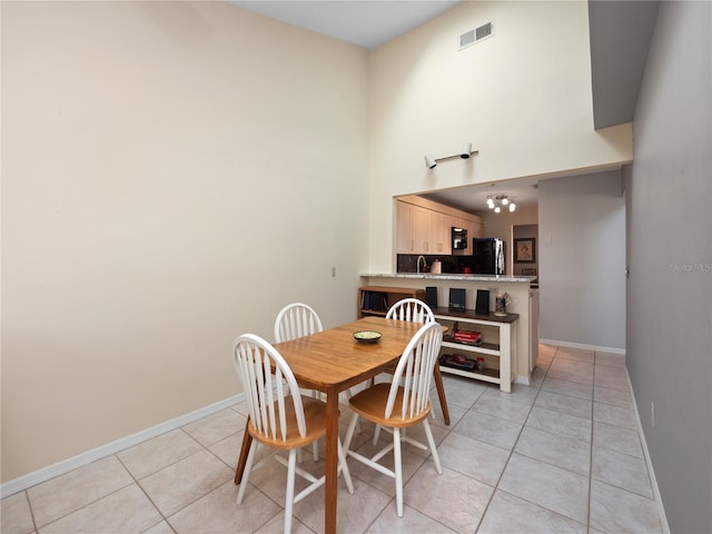 dining room featuring light tile patterned flooring, a towering ceiling, visible vents, and baseboards