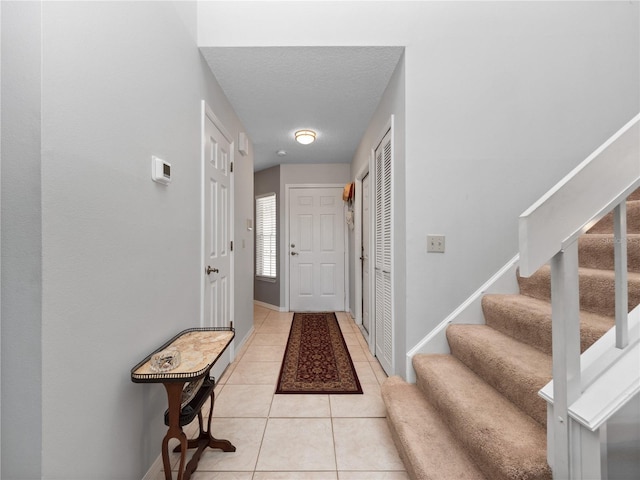 interior space featuring light tile patterned floors, baseboards, stairway, and a textured ceiling