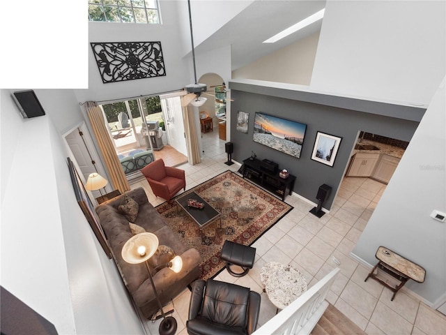 living area with light tile patterned floors, a skylight, a towering ceiling, and baseboards