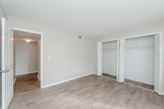 unfurnished bedroom with light wood-type flooring, a textured ceiling, and multiple closets