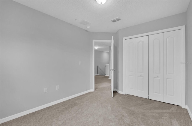 unfurnished bedroom featuring a textured ceiling, a closet, and light carpet