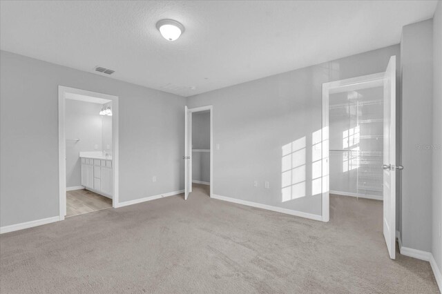 unfurnished bedroom with light carpet, a closet, a textured ceiling, and ensuite bath