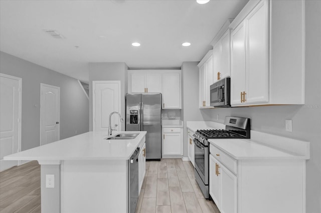 kitchen with white cabinets, stainless steel appliances, light hardwood / wood-style floors, sink, and a center island with sink