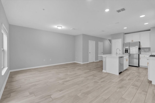 kitchen with white cabinets, appliances with stainless steel finishes, light hardwood / wood-style floors, and a center island with sink