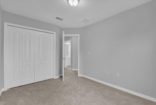 unfurnished bedroom featuring light carpet, a closet, and a textured ceiling