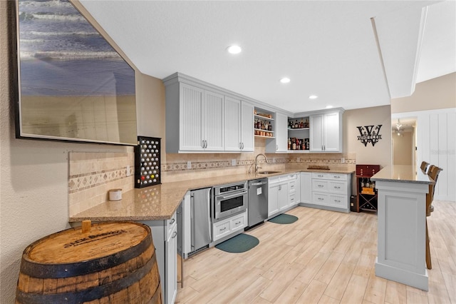 kitchen with sink, tasteful backsplash, kitchen peninsula, light stone countertops, and appliances with stainless steel finishes