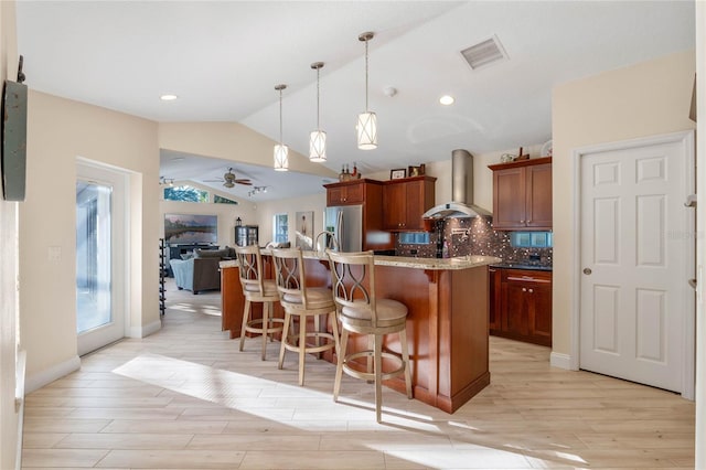 kitchen with vaulted ceiling, backsplash, stainless steel fridge, wall chimney range hood, and pendant lighting