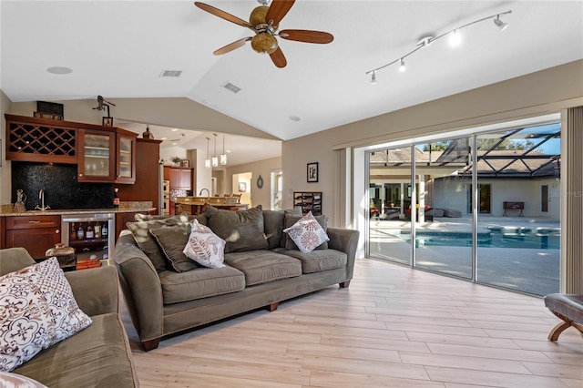 living room featuring light hardwood / wood-style flooring, lofted ceiling, beverage cooler, wet bar, and ceiling fan