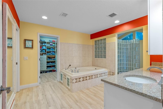 bathroom with wood-type flooring, vanity, and a relaxing tiled tub