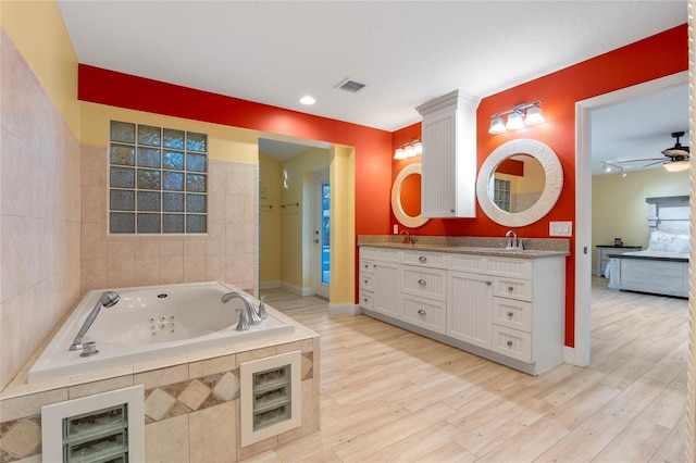 bathroom featuring ceiling fan, tiled tub, vanity, and wood-type flooring