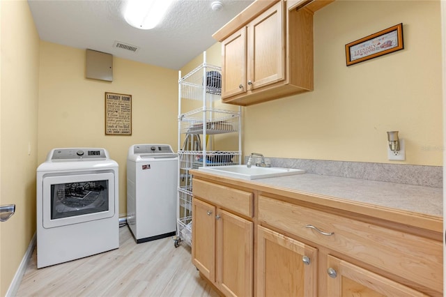 laundry room with sink, a textured ceiling, washing machine and clothes dryer, cabinets, and light hardwood / wood-style floors